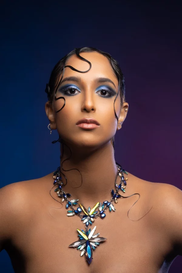 Femme brune maquillage noir et bleu collier gros strass fond bleu marine